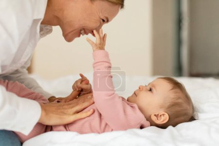 Téléchargez les photos : Loving mom playing with baby girl at home, enjoying motherhood and maternity leave, cute infant child touching happy mothers face, pushing nose and smiling - en image libre de droit