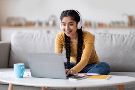 Photo for Remote Education. Young Indian Woman In Headphones Studying With Laptop At Home, Smiling Hindu Female Student Using Computer For Distance Learning While Sitting On Couch In Living Room, Free Space - Royalty Free Image