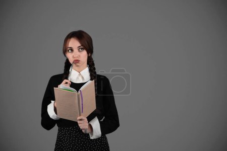 Foto de Chica inteligente pensativa estudiante en ropa negra gótica con coletas con libro, se le ocurrió y mirar el espacio vacío, aislado en el fondo del estudio gris. Tormenta de ideas, diario de sueños, estudio y planificación del día - Imagen libre de derechos