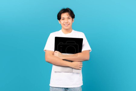 Téléchargez les photos : Asian Teen Guy Holding Hugging Laptop With Blank Screen Advertising Website Standing Over Blue Background. Studio Shot Of Boy Posing With Computer. Technology And Gadgets Concept - en image libre de droit