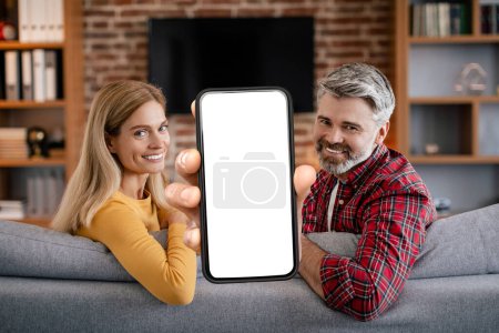 Photo for Cool App. Portrait of happy middle aged couple demonstrating smartphone with empty screen in hand, showing device with blank space for mockup while relaxing together on couch at home, collage - Royalty Free Image