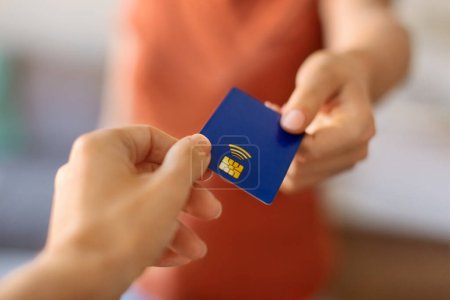 Photo for Closeup shot of young woman giving blue credit card to female hand, pov of unrecognizable lady passing bank card to client, offering financial services or paying for shopping, selective focus - Royalty Free Image