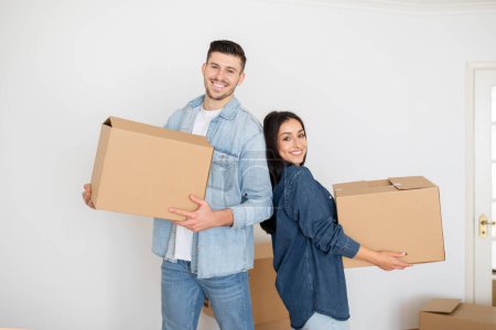 Photo for Happy Young Couple Carrying Boxes Into New Home On Moving Day, Cheerful Millennial Spouses Posing With Belongings In Hands And Smiling At Camera, Enjoying Relocation To Own House, Copy Space - Royalty Free Image