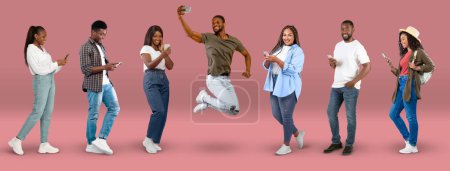 Téléchargez les photos : Happy millennial black people in casual chatting on smartphone, taking selfie, jump, on pink background, studio, panorama, full length. Device, app for blog and social networks, great news and sale - en image libre de droit