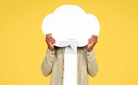Téléchargez les photos : Adult black man in casual hold abstract bubble, cloud for thoughts and words with free space for text on face, isolated on yellow background, studio, unrecognizable. Ad and offer, sale recommendation - en image libre de droit
