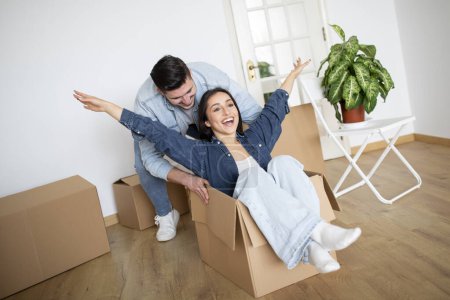 Photo for Happy Couple Having Fun With Cardboard Boxes At Home In Moving Day, Cheerful Young Spouses Fooling Together And Laughing While Unpacking, Celebrating Relocation To Their New Apartment - Royalty Free Image