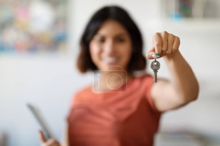Retrato de sonriente joven agente de bienes raíces femenino sosteniendo portapapeles y mostrando las llaves caseras en la mano, Gerente de la propiedad mujer bienvenida en la nueva casa, recomendando programas hipotecarios, enfoque selectivo