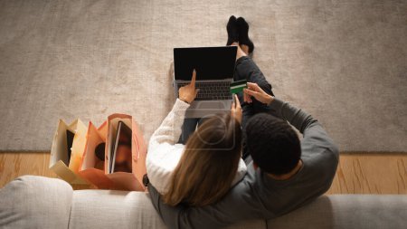 Photo for Young arab man hug european wife, ordering purchase on computer with blank screen, enjoy online shopping in living room interior with packages. Love, relationship, sale and cashback together at home - Royalty Free Image