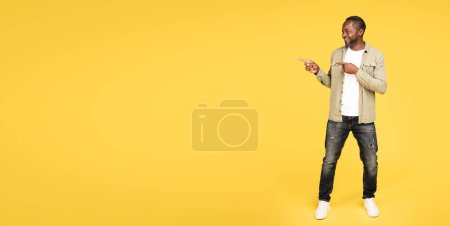 Photo for Glad calm mature black male in casual show fingers at empty space, recommend ad and offer, isolated on orange studio background, full length, panorama. Professional advice, good news and positive - Royalty Free Image