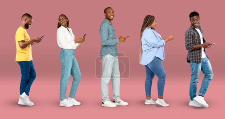 Téléchargez les photos : Cheerful young african american women and men in casual typing on smartphones, watch video on pink background, studio, panorama. App for communication and chat online, social media technology and blog - en image libre de droit