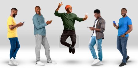 Foto de Smiling young black guys in casual typing on smartphones jumping, take selfie on white background, studio, panorama. App for blog, social networks, communication online, technology for spare time - Imagen libre de derechos