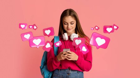 Téléchargez les photos : Cheerful teen european woman student with backpack has romantic chat with hearts on smartphone, enjoys message on pink studio background, panorama. App for dating remotely, relationships and love - en image libre de droit