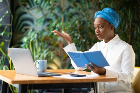 Photo for Irritated unhappy young black lady in smart casual and blue turban manager have online meeting with colleagues, looking at laptop screen and gesturing, hold notepad, scolding employees, cafe interior - Royalty Free Image