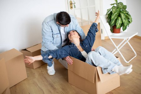 Photo for Young Couple Having Fun While Relocating Home, Man Pushing Cardboard Box With His Happy Wife, Cheerful Spouses Fooling Together While Unpacking Things After Moving To New Apartment, Closeup - Royalty Free Image