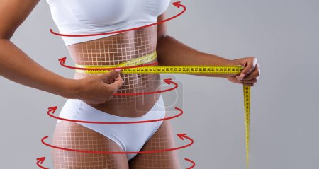 Téléchargez les photos : Young slim black female in white lingerie with abstract lines, arrows check waist with measuring tape isolated on gray background, studio. Anticellulite massage, beauty care, diet and weight loss - en image libre de droit