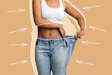 Téléchargez les photos : Millénaire mince dame afro-américaine en gros jeans profiter d'un résultat de perte de poids avec graisse corps abstrait autour et des flèches isolées sur fond de mur beige, studio. Soins de beauté, alimentation, avant et après - en image libre de droit