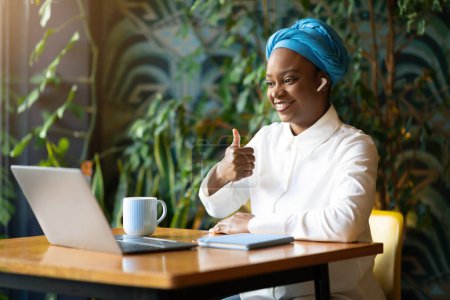 Photo for Attractive happy friendly millennial black woman in smart casual sitting at desk in front of pc laptop, showing thumb up at computer screen and smiling, have online meeting with client, copy space - Royalty Free Image