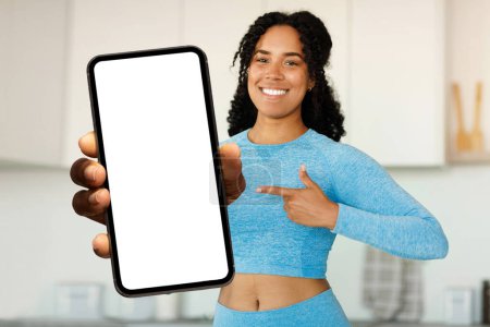 Photo for Fitness App. Sporty Black Woman Pointing At Big Blank Smartphone In Hand, Happy Young African American Lady In Sportswear Recommending Workout Application, Or Website, Collage, Mockup - Royalty Free Image