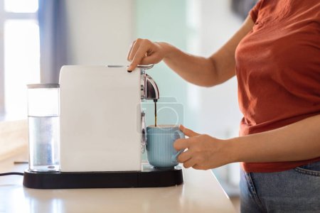 Foto de Unrecognizable Woman Turning On Coffee Machine While Preparing Morning Drink In Kitchen, Young Female Using Modern Appliance At Home, Filling Mug With Caffeine Beverage, Cropped Shot, Side View - Imagen libre de derechos