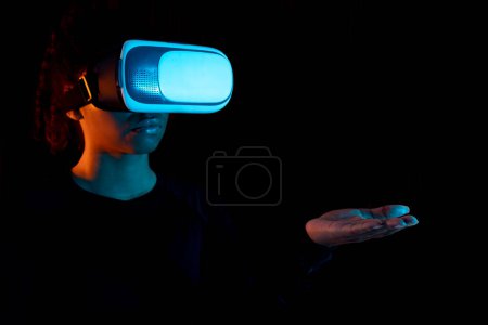 Photo for Black lady in vr glasses presenting invisible object on her palm hand, space for design, free copy space. Woman having virtual reality eyeglasses and showing crutial informations - Royalty Free Image