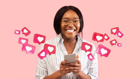 Foto de Feliz joven hembra negra tiene una charla romántica con los corazones en el teléfono inteligente, disfrutar del mensaje en las redes sociales en el fondo del estudio rosa, panorama. Aplicación para la comunicación, citas remotas, relación y amor - Imagen libre de derechos