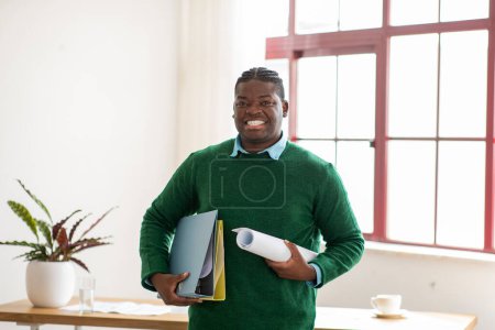 Photo for Happy African American Architect Man Standing Holding Rolled Up Paper Drawings And Folders With Projects Posing Smiling To Camera In Modern Office. Professional Design And Engineering Career - Royalty Free Image