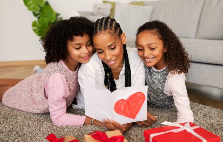 Photo for Mothers Day Holiday. Cheerful African American Daughters Congratulating Their Mom On Birthday Giving Her Painted Card And Presents Lying On Floor At Home. Family Celebrating Special Date Concept - Royalty Free Image
