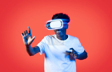 Photo for African american guy user checking newest VR glasses on red background in neon light, happy young black man experiencing virtual reality, playing video game, have meta quest experience - Royalty Free Image