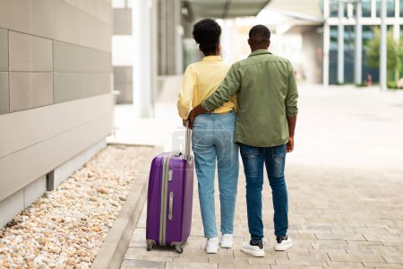 Téléchargez les photos : Vue arrière du couple afro-américain marchant avec une valise de voyage et embrassant profiter des vacances à l'aéroport à l'extérieur. Tournage complet de touristes méconnaissables. Concept de transport - en image libre de droit