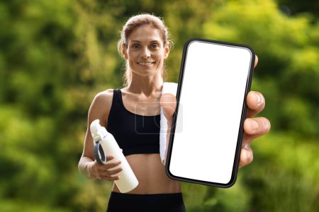 Photo for Sport App. Athletic Middle Aged Female Demonstrating Blank Smartphone At Camera While Jogging Outdoors In City Park, Sporty Woman Recommending New Application Or Website, Collage, Mockup - Royalty Free Image