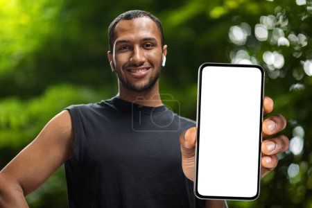 Photo for Sport App. Athletic Black Guy Demonstrating Blank Cellphone At Camera While Jogging Outdoors In City Park, Sporty African American Man Showing Smartphone With Empty Screen For Mockup, Collage - Royalty Free Image