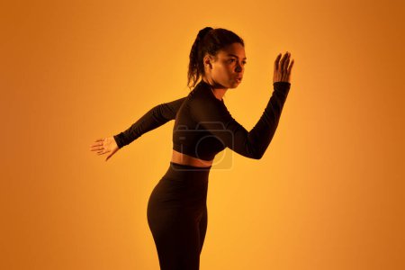 Photo for Portrait of determined black woman exercising, running over orange neon background, studio shot, free space. Sport lifestyle concept - Royalty Free Image