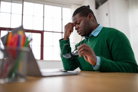 Photo for Eye Fatigue. Tired Black Male Having Sore Eyes Suffering From Glaucoma Symptoms Working On Laptop Holding His Glasses And Rubbing Nosebridge In Modern Office. Eyesight Issues Concept - Royalty Free Image