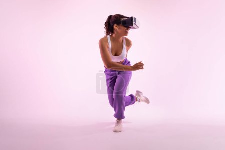 Foto de Mujer negra alegre disfrutando de la experiencia de realidad virtual en auriculares vr modernos, ajuste joven dama disfrutando de clase de fitness 3D sobre fondo de luz de neón rosa, espacio de copia - Imagen libre de derechos