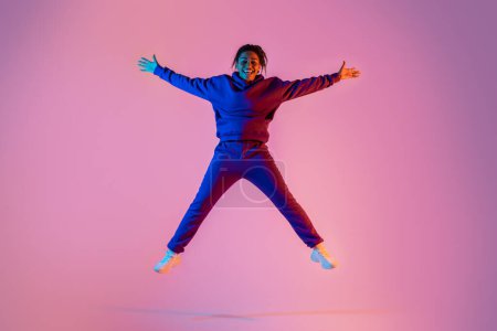 Téléchargez les photos : Longueur totale du corps de la jeune femme sportive afro-américaine sautant en forme d'étoile, s'amusant sur fond de studio couleur néon rose, pleine longueur, espace libre - en image libre de droit