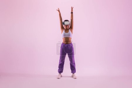 Téléchargez les photos : Dame noire sportive expérience de la réalité virtuelle fitness dans le casque vr, regarder tutoriel d'entraînement et échauffement sur fond de lumière rose néon, faire de l'exercice en métaverse - en image libre de droit