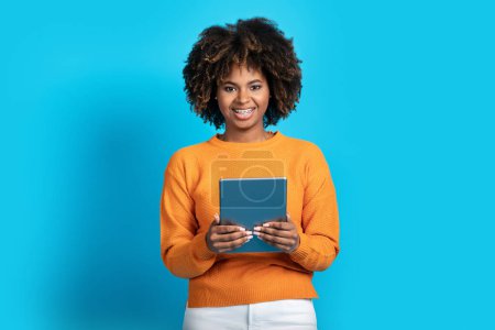 Photo for Happy attractive curly young black woman with teeth braces using modern digital pc pad on blue studio background and smiling, checking newest educational or entertaining app, copy space - Royalty Free Image