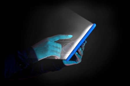 Téléchargez les photos : Femme tenant smartphone avec écran blanc brillant sur fond sombre avec lumière au néon, vue latérale, gros plan. Dame méconnaissable surfant sur Internet ou textos - en image libre de droit