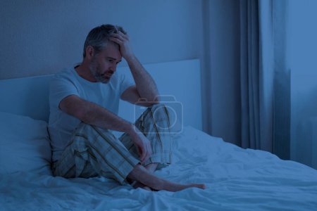 Photo for Sleep disorders. Stressed upset thoughtful handsome middle aged man wearing pajamas sitting on bed at night, touching head, awake from bad dream, suffering from nightmares, home interior, copy space - Royalty Free Image