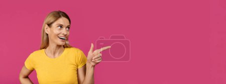 Téléchargez les photos : Femme européenne adulte souriante avec bouche ouverte pointant du doigt l'espace vide, isolée sur fond violet, studio, gros plan, panorama. Choix, offre choquante et annonce, vente énorme et émotions des gens - en image libre de droit