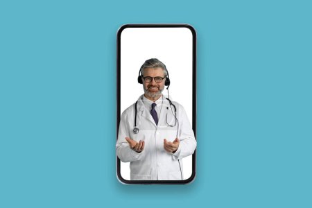 Téléchargez les photos : Joyeux amical beau cheveux gris médecin d'âge moyen avec casque dans grand téléphone portable gestuelle et souriant à la caméra, ont rendez-vous en ligne, fond bleu, collage, espace de copie - en image libre de droit