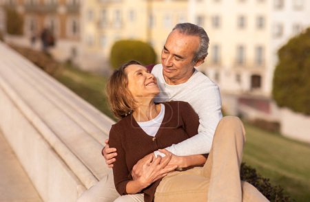 Photo for Happy Senior Couple Hugging Sitting Enjoying Weekend Outdoors. Retired Spouses Traveling And Embracing Spending Time Together Outside. Long Lasting Marriage And Retired Lifestyle Concept - Royalty Free Image