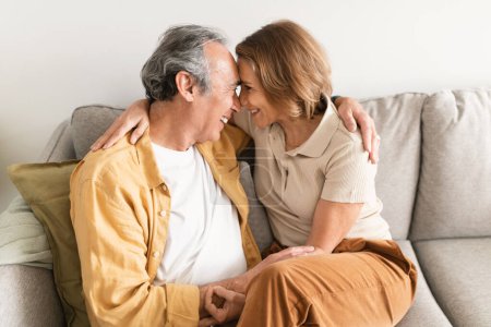Photo for Loving senior european man and his wife looking at each other and touching foreheads, talking, enjoying free time in living room interior. Love, couple relationship, romance and family at home - Royalty Free Image