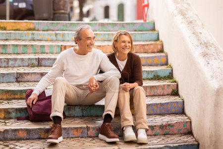Photo for Happy Retirement And Vacation. Senior Tourists Couple Sitting On Colorful Steps Outdoors Resting During Walking Tour In European City. Mature Travelers Enjoying Sightseeing - Royalty Free Image