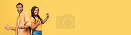 Foto de Emocional afroamericano joven hombre y mujer haciendo gestos y bailando sobre fondo de estudio amarillo, pareja negra enamorada celebrando el éxito, panorama con espacio de copia para el anuncio, collage - Imagen libre de derechos