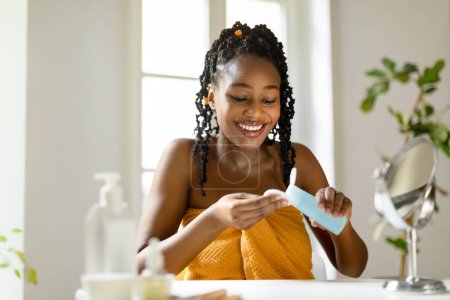 Photo for Happy black lady pouring micellar water on cotton pad, making beauty routine at home and smiling, free space. Positive woman cleansing face from makeup - Royalty Free Image