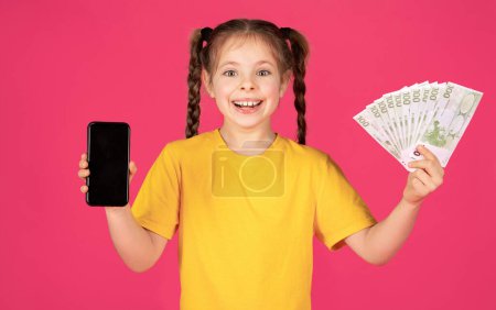 Photo for Happy Excited Little Girl Showing Blank Smartphone And Euro Cash Money At Camera, Cute Preteen Female Child Advertising Online Offer While Standing Isolated Over Pink Background, Mockup - Royalty Free Image