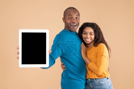 Photo for New app. Happy black couple showing digital tablet with mockup, promoting application or website, advertising your product or service, beige studio background, mockup - Royalty Free Image