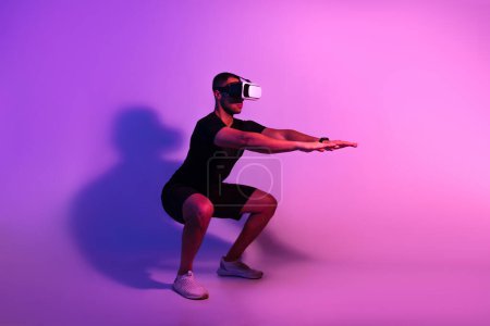 Foto de Aplicación VR Workout. Deportivo hombre negro con auriculares de realidad virtual Ejercicio haciendo sentadillas profundas sobre fondo de estudio de neón púrpura. Concepto moderno de deporte y tecnología. Vista lateral - Imagen libre de derechos
