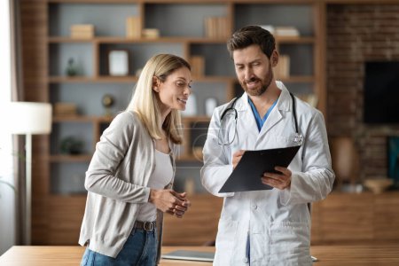 Photo for Smiling Male Doctor Discussing Medical Treatment To Female Patient During Meeting In Clinic Office, Friendly Therapist Man Holding Clipboard, Showing Prescription Details To Smiling Lady - Royalty Free Image